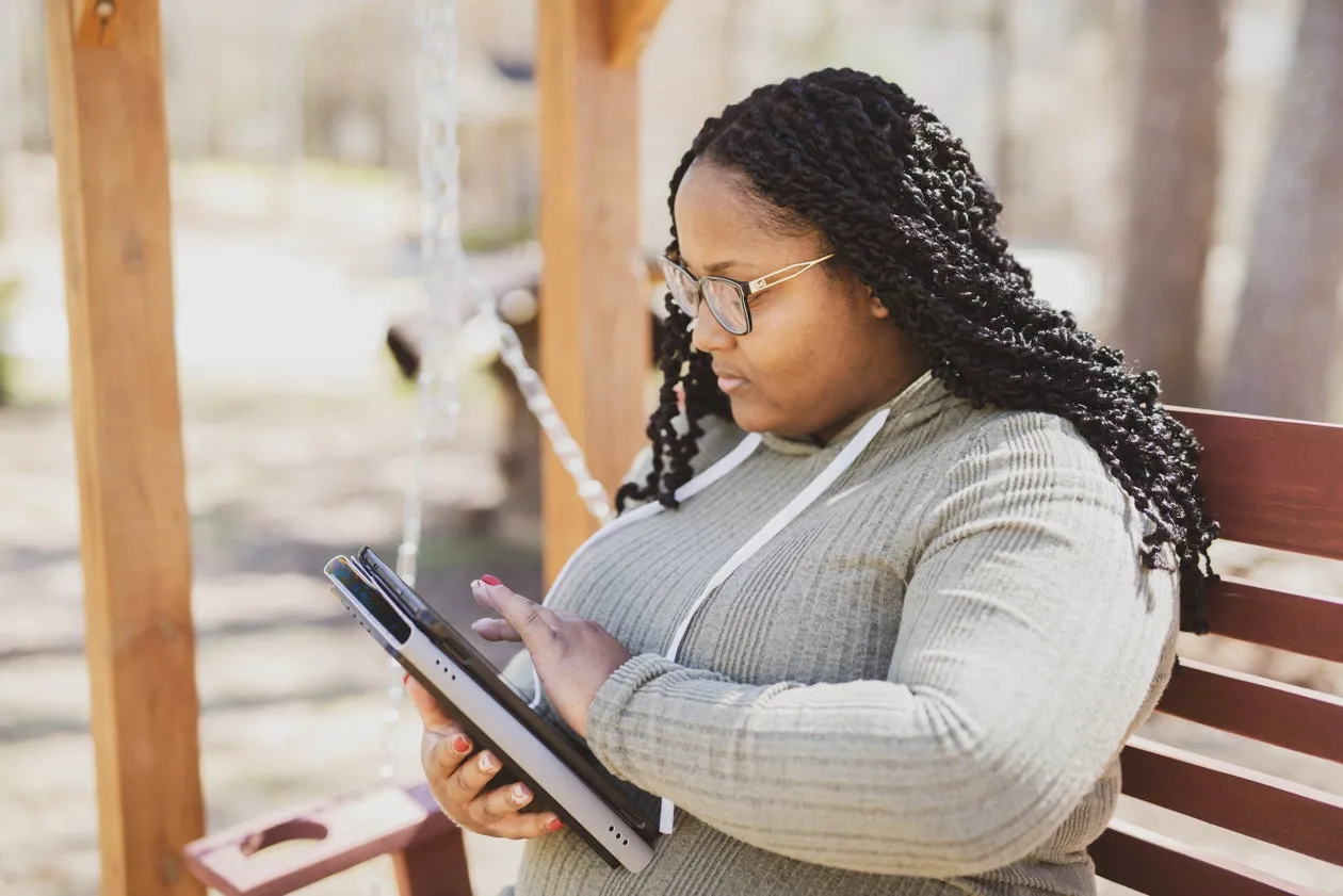 A woman sitting on a porch swing, browsing on her tablet outdoors